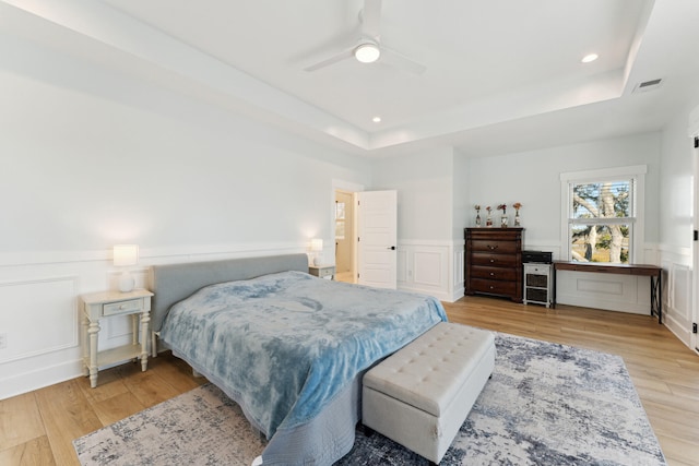 bedroom featuring a raised ceiling, ceiling fan, and light wood-type flooring