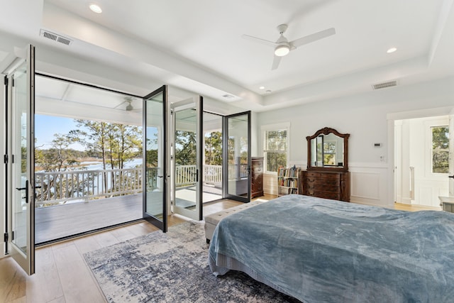 bedroom with ceiling fan, access to outside, light hardwood / wood-style floors, and a tray ceiling