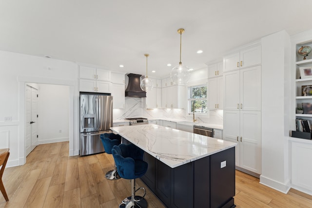 kitchen with appliances with stainless steel finishes, white cabinetry, a kitchen island, decorative light fixtures, and custom exhaust hood