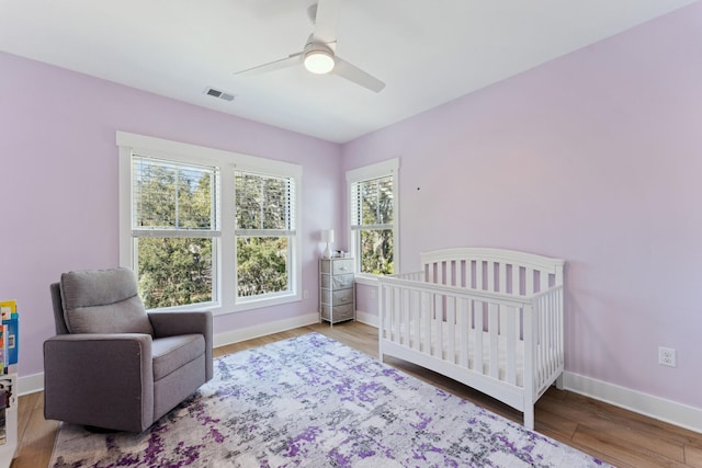 bedroom featuring hardwood / wood-style flooring, a crib, and ceiling fan