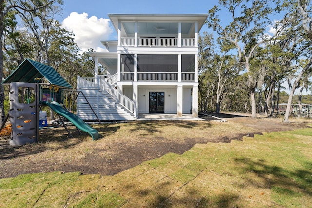 rear view of house with a playground, a sunroom, and a yard