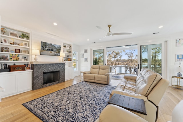 living room featuring built in shelves, ceiling fan, a fireplace, and light hardwood / wood-style flooring