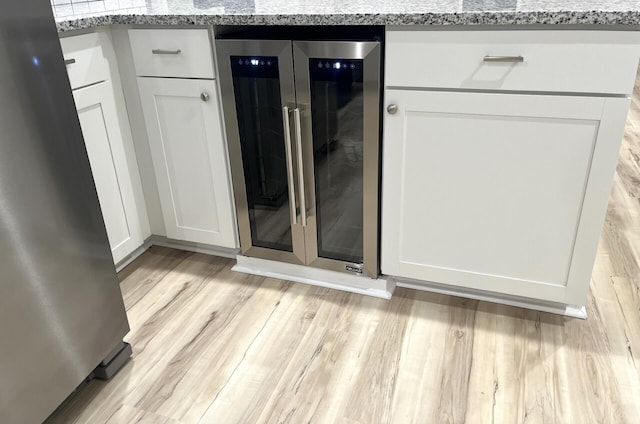 room details with white cabinets, beverage cooler, light stone counters, and light hardwood / wood-style flooring