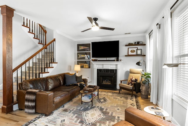 living room with light wood-type flooring, ceiling fan, a premium fireplace, and ornamental molding