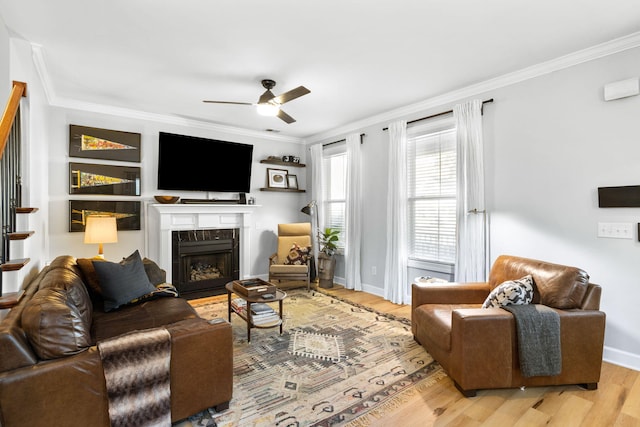 living room with light wood-type flooring, ceiling fan, a premium fireplace, and ornamental molding