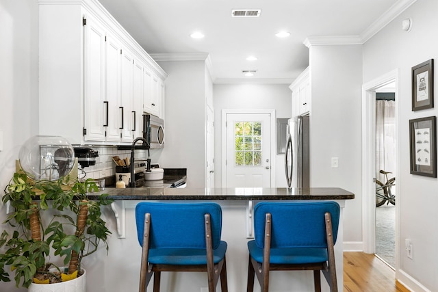 kitchen featuring white cabinets, stainless steel appliances, kitchen peninsula, light hardwood / wood-style flooring, and a breakfast bar area