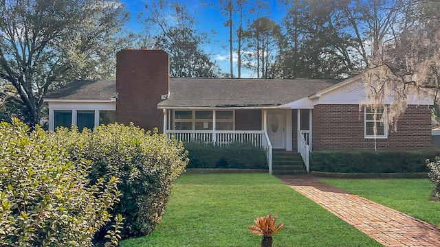 single story home featuring a front yard, a chimney, a porch, and brick siding