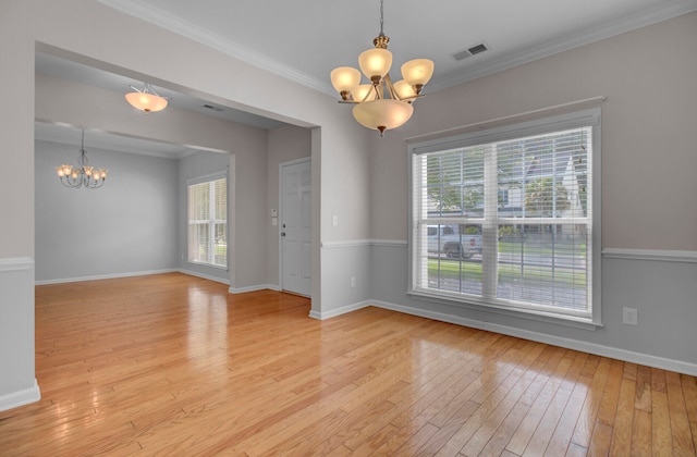 empty room with a notable chandelier, ornamental molding, and light hardwood / wood-style flooring