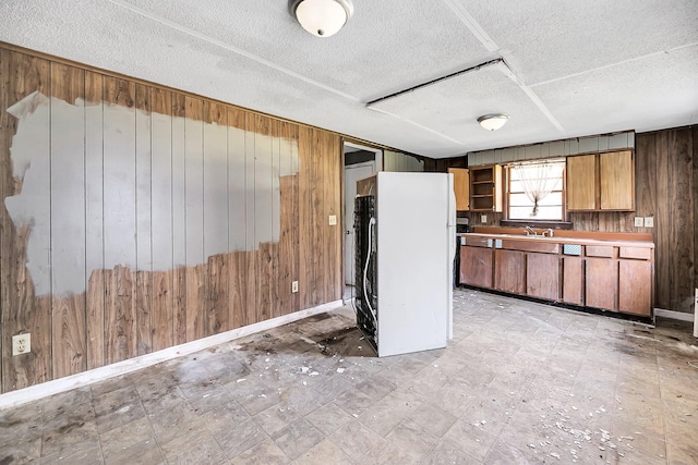 kitchen featuring wooden walls, white fridge, and a textured ceiling