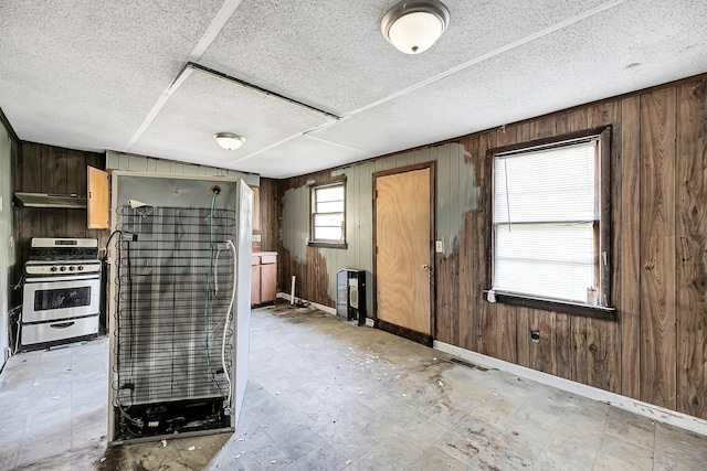 kitchen with wood walls, gas range oven, a textured ceiling, and ventilation hood