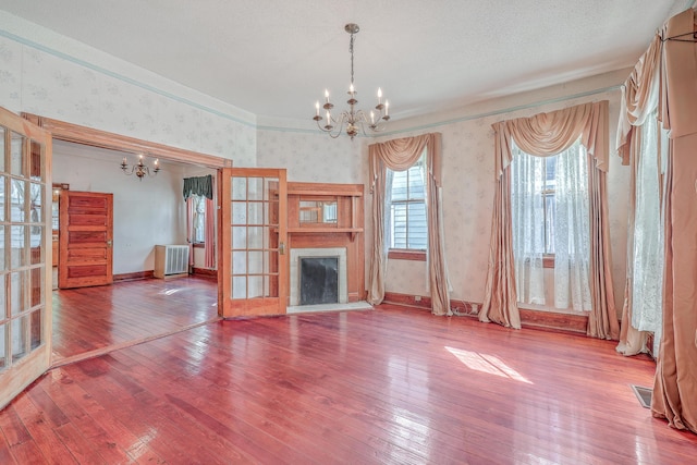 unfurnished living room with a notable chandelier, radiator, a textured ceiling, and hardwood / wood-style floors