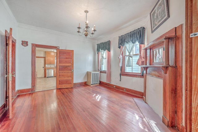 spare room featuring radiator, hardwood / wood-style flooring, crown molding, and a chandelier