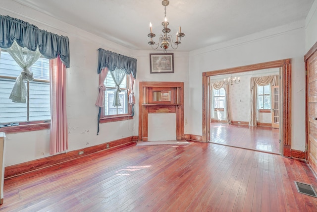 unfurnished living room with hardwood / wood-style floors, an inviting chandelier, and plenty of natural light