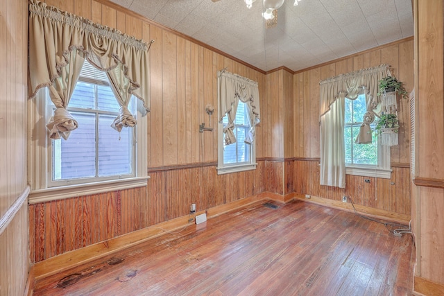 empty room featuring ornamental molding, hardwood / wood-style floors, and wood walls