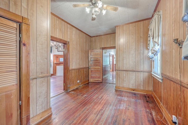 spare room with ceiling fan, crown molding, dark hardwood / wood-style flooring, and wood walls