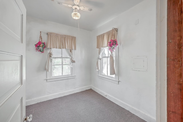 empty room with ceiling fan, dark colored carpet, and a healthy amount of sunlight