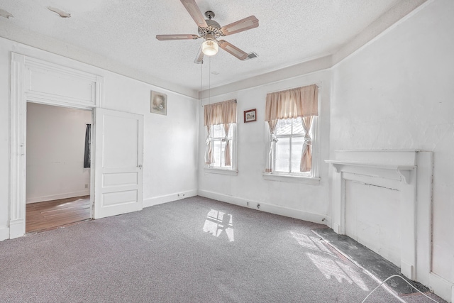 interior space with a fireplace, ceiling fan, dark colored carpet, and a textured ceiling