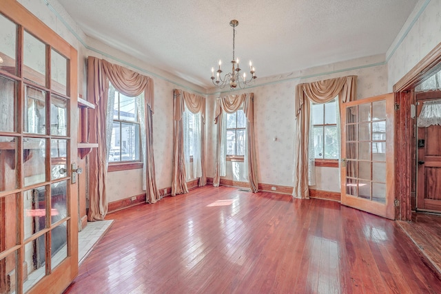 unfurnished dining area with an inviting chandelier, hardwood / wood-style flooring, and a textured ceiling