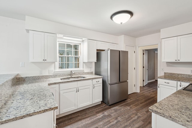 kitchen featuring dark wood-style flooring, light stone countertops, a sink, freestanding refrigerator, and white cabinetry