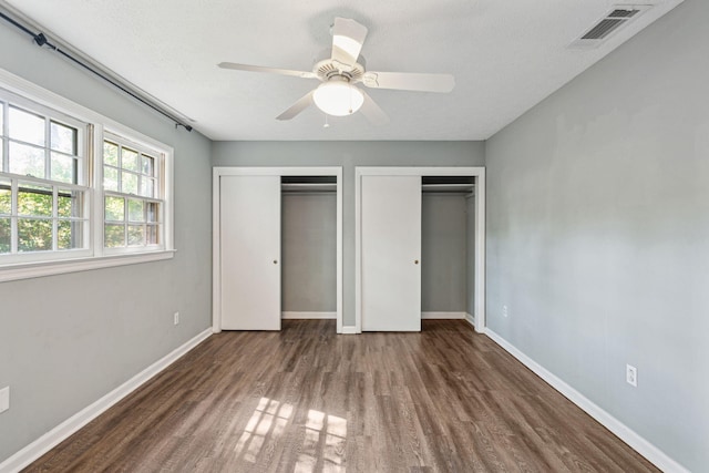 unfurnished bedroom with visible vents, two closets, wood finished floors, baseboards, and ceiling fan