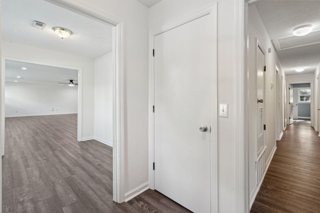 hallway with visible vents, attic access, dark wood-style flooring, and baseboards