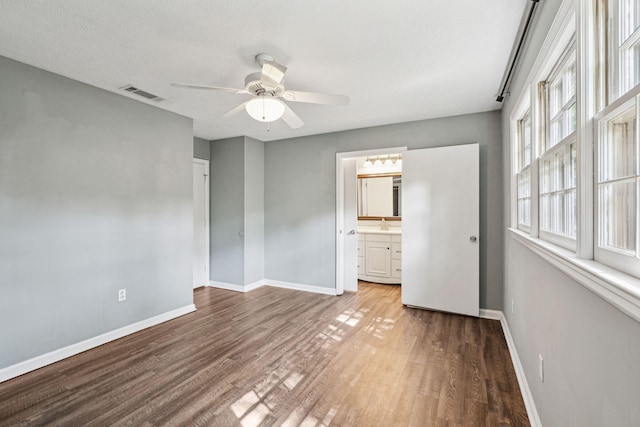 unfurnished bedroom featuring visible vents, connected bathroom, baseboards, and wood finished floors