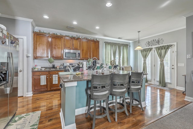 kitchen with a breakfast bar, ornamental molding, brown cabinets, stainless steel appliances, and dark wood-type flooring