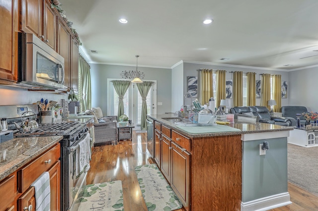 kitchen featuring crown molding, light wood finished floors, brown cabinets, open floor plan, and stainless steel appliances