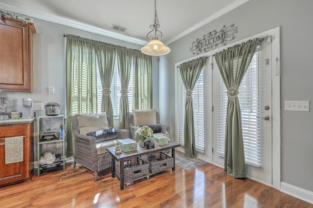 living area with light wood-style flooring, visible vents, ornamental molding, and a wealth of natural light