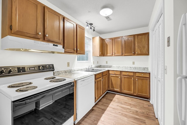 kitchen with a textured ceiling, light wood-type flooring, white appliances, and sink