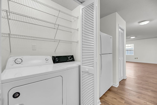 laundry area featuring a textured ceiling, washing machine and dryer, and light hardwood / wood-style floors