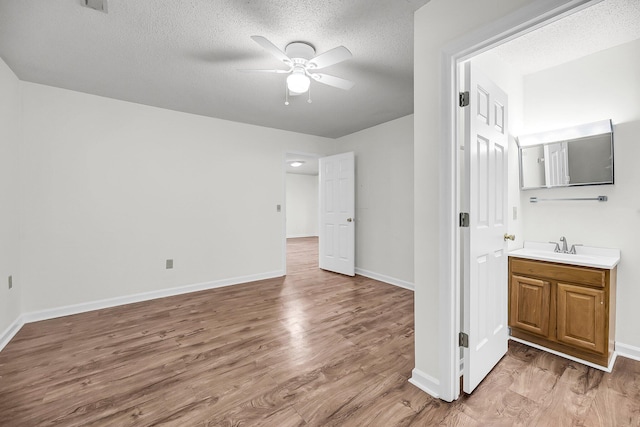 unfurnished bedroom with a textured ceiling, connected bathroom, light hardwood / wood-style floors, and ceiling fan