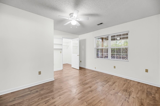 unfurnished bedroom with hardwood / wood-style flooring, ceiling fan, a walk in closet, and a textured ceiling