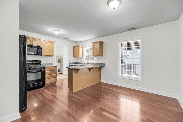 kitchen featuring black appliances, a kitchen bar, kitchen peninsula, and dark wood-type flooring