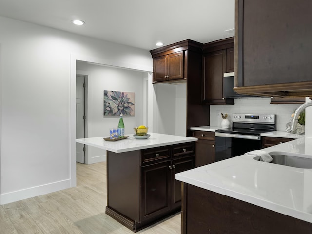 kitchen with electric stove, backsplash, dark brown cabinetry, a sink, and light wood-type flooring