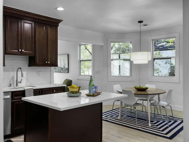 kitchen with decorative light fixtures, tasteful backsplash, stainless steel dishwasher, a sink, and dark brown cabinets