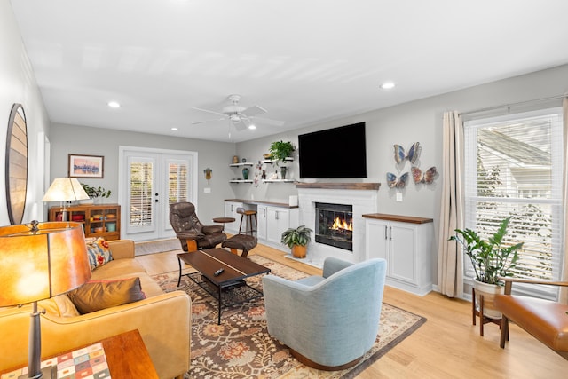 living room featuring light wood-style floors, a brick fireplace, french doors, and plenty of natural light