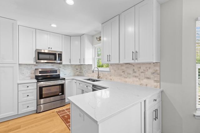 kitchen with stainless steel appliances, a sink, white cabinetry, light wood finished floors, and tasteful backsplash