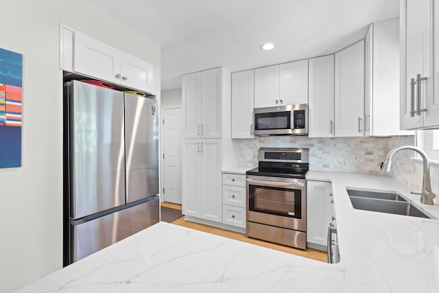 kitchen featuring appliances with stainless steel finishes, white cabinetry, a sink, and light stone countertops