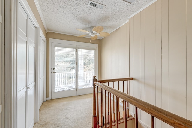 corridor featuring ornamental molding, a textured ceiling, light colored carpet, and wood walls