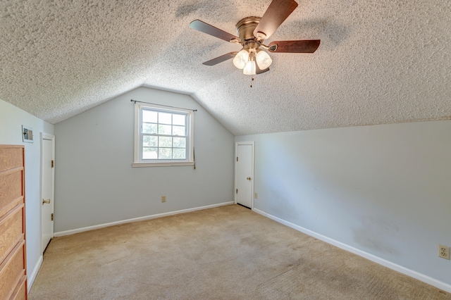 additional living space with a textured ceiling, vaulted ceiling, light colored carpet, and ceiling fan