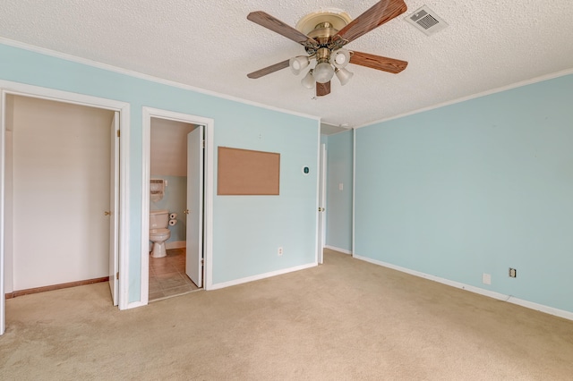 unfurnished bedroom with light carpet, ceiling fan, a textured ceiling, crown molding, and ensuite bath