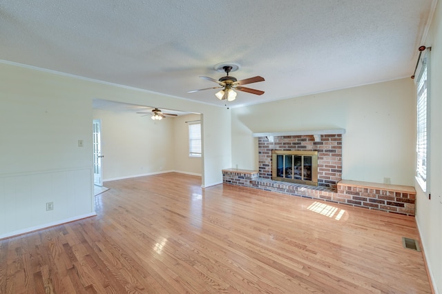 unfurnished living room with light hardwood / wood-style flooring, a textured ceiling, a fireplace, and crown molding