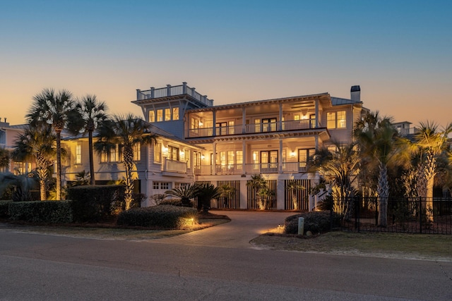 coastal home featuring a balcony, a chimney, fence, and decorative driveway