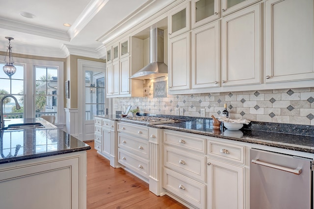 kitchen with a sink, wall chimney exhaust hood, light wood finished floors, a tray ceiling, and crown molding