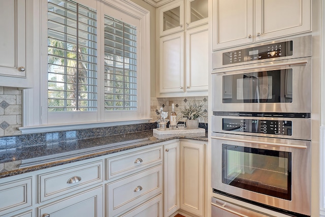 kitchen with double oven, a warming drawer, decorative backsplash, dark stone counters, and glass insert cabinets