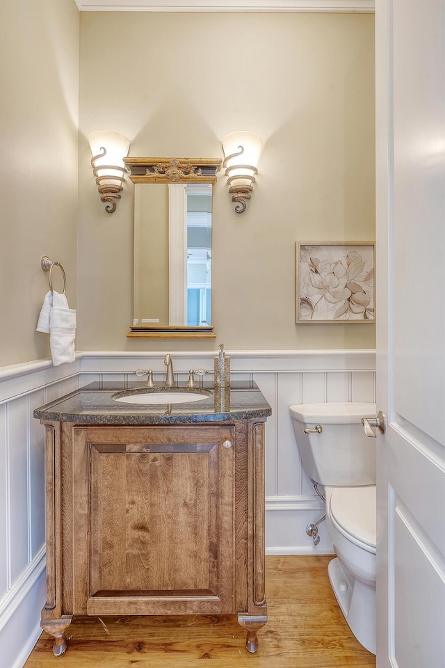 half bath featuring toilet, a wainscoted wall, wood finished floors, and vanity