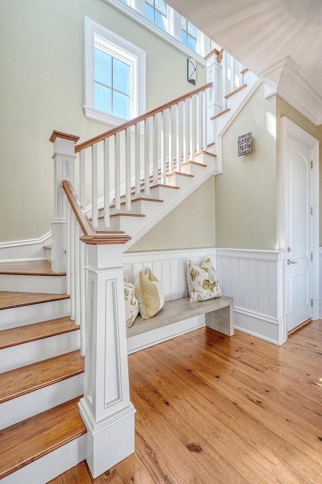 stairs featuring wood finished floors and wainscoting