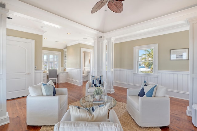 living area with a ceiling fan, a wainscoted wall, decorative columns, and wood finished floors