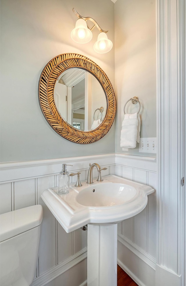 half bath featuring toilet, a decorative wall, and wainscoting